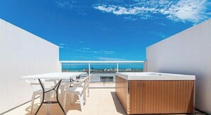Eine Dachterrasse mit einem weißen Tisch und Stühlen, einer Holz-Whirlpool und Blick auf die Stadtlandschaft.