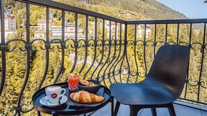 Un balcón con una mesa dispuesta para el desayuno, que incluye un croissant, un vaso de jugo y una taza de café.