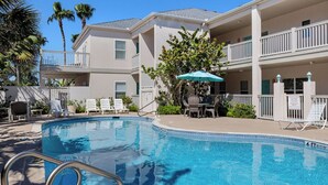 A swimming pool with lounge chairs and umbrellas, surrounded by a two-story building with balconies. - Charming 3BR/2BA - 1/2 Block to Beach - Sleeps 8 from Rent On Padre (South Padre Island)