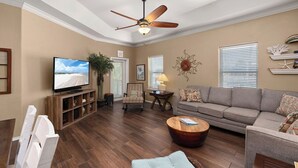 A living room with a ceiling fan, a television, a sofa, a coffee table, and a dining area with chairs. - Charming 3BR/2BA - 1/2 Block to Beach - Sleeps 8 from Rent On Padre (South Padre Island)