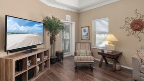 A living room with a flat-screen TV, a chair, a small table with a lamp, and a potted plant. - Charming 3BR/2BA - 1/2 Block to Beach - Sleeps 8 from Rent On Padre (South Padre Island)