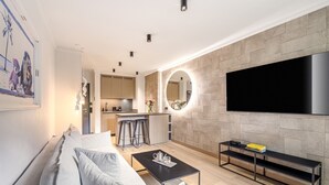 Una sala moderna con sofá, mesa de centro, televisor y cocina al fondo.