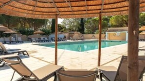 Un espace piscine doté de chaises longues et d’une structure en forme de parasol recouverte de chaume.