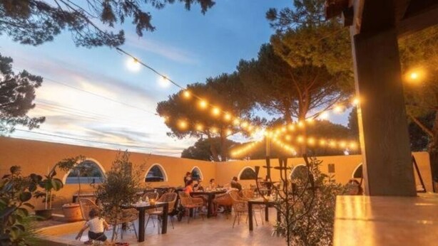 Un espace extérieur aménagé en terrasse, avec des tables et des chaises, des guirlandes lumineuses et des plantes en pot.