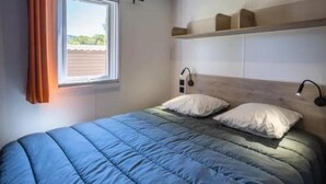 Une chambre à coucher avec un lit, deux lampes de chevet, une fenêtre avec des rideaux et une étagère au-dessus du lit.