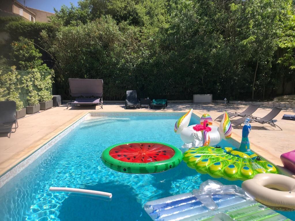 Une piscine avec des jeux gonflables, des chaises longues et une haie en arrière-plan.