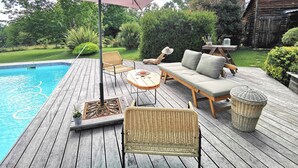 Une terrasse en bois avec une piscine, des meubles en osier et un grand parasol pour faire de l’ombre.