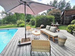 A wooden deck with a pool, wicker furniture, and a large umbrella providing shade. - 8, family or friends, share the Pyrenees (Villeneuve-de-Rivière)