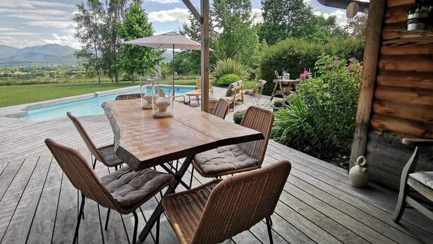 Une terrasse extérieure avec une table en bois et des chaises en osier, donnant sur une piscine et une végétation luxuriante.