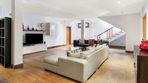 Una sala de estar moderna con un sofá grande, un televisor de pantalla plana y una escalera que sube a un piso superior.