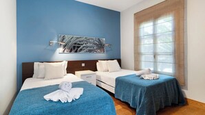 Habitación de hotel con dos camas, un ventanal con persianas, una obra de arte en la pared y suelo de madera.