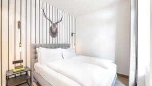 Une chambre d’hôtel moderne avec un grand lit, une table de chevet avec une lampe et une décoration murale représentant une tête de cerf.