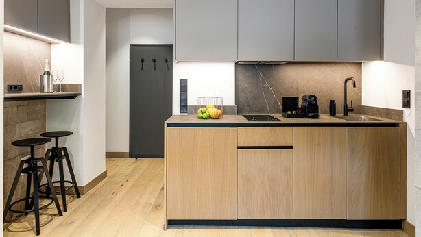 Une cuisine moderne avec des meubles en bois, un four encastré, un évier et deux tabourets.