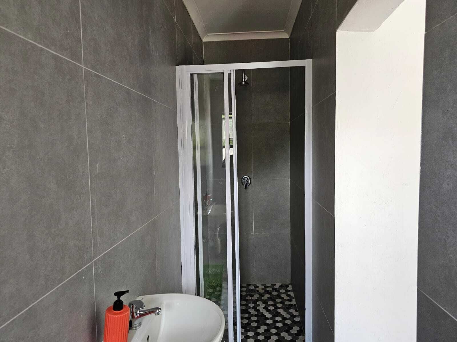 A modern bathroom with a glass-enclosed shower, a white sink with a red soap dispenser, and a black and white patterned floor.