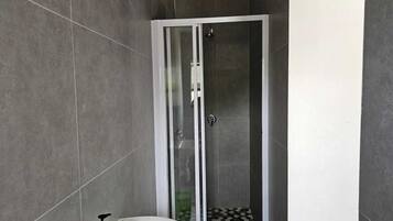 A modern bathroom with a glass-enclosed shower, a white sink with a red soap dispenser, and a black and white patterned floor.