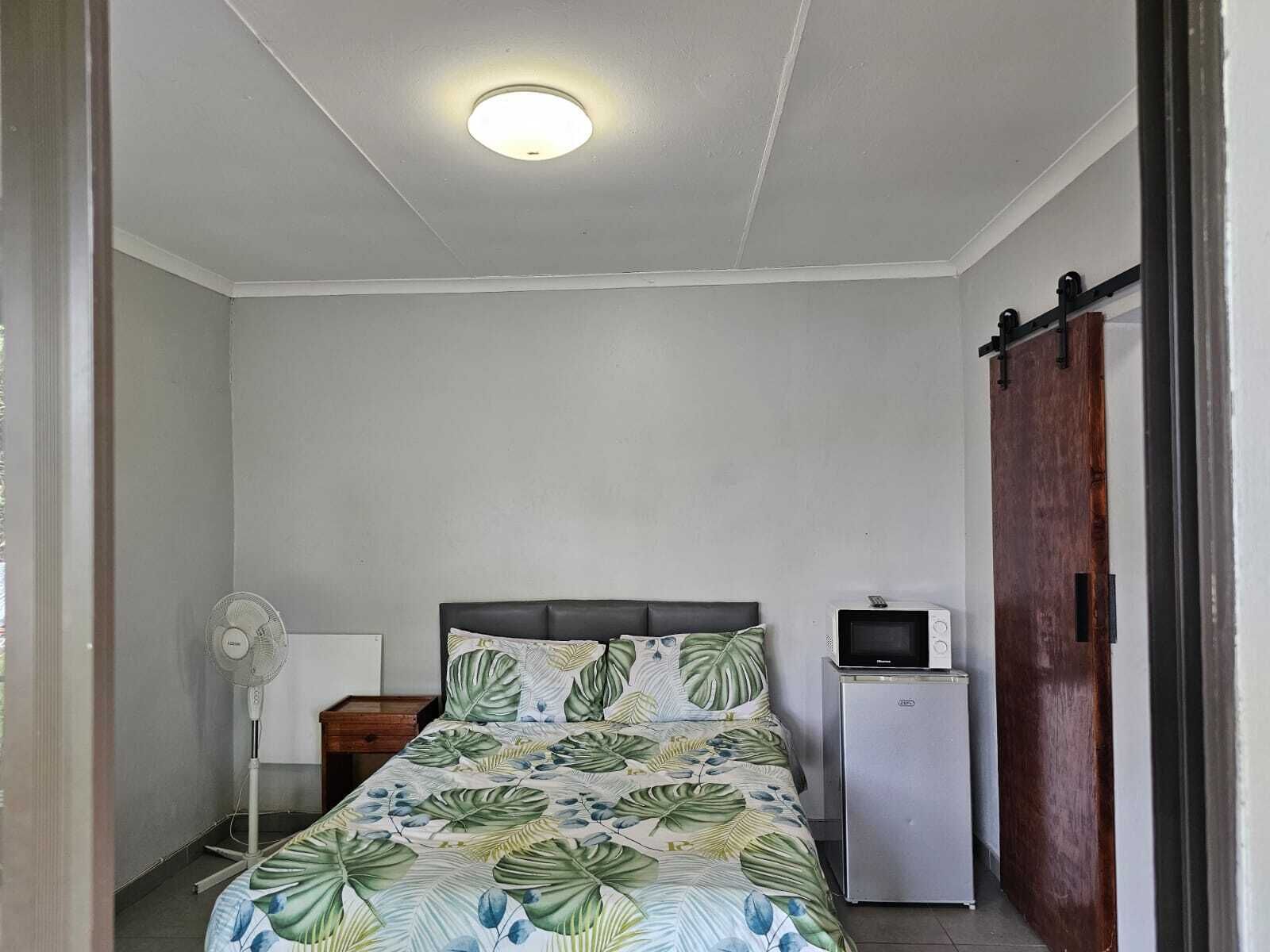 Une chambre avec un lit, un ventilateur, un petit réfrigérateur et une armoire en bois.
