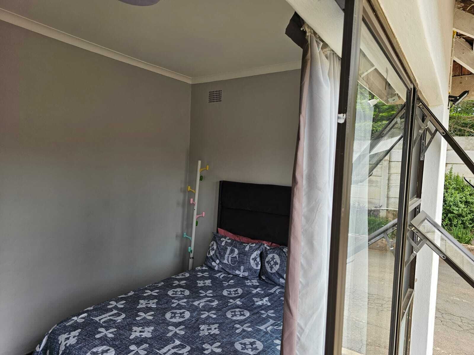 Ein kleines Schlafzimmer mit einem Einzelbett, einem Fenster mit Vorhang und einem Balkon mit Metallgitter.