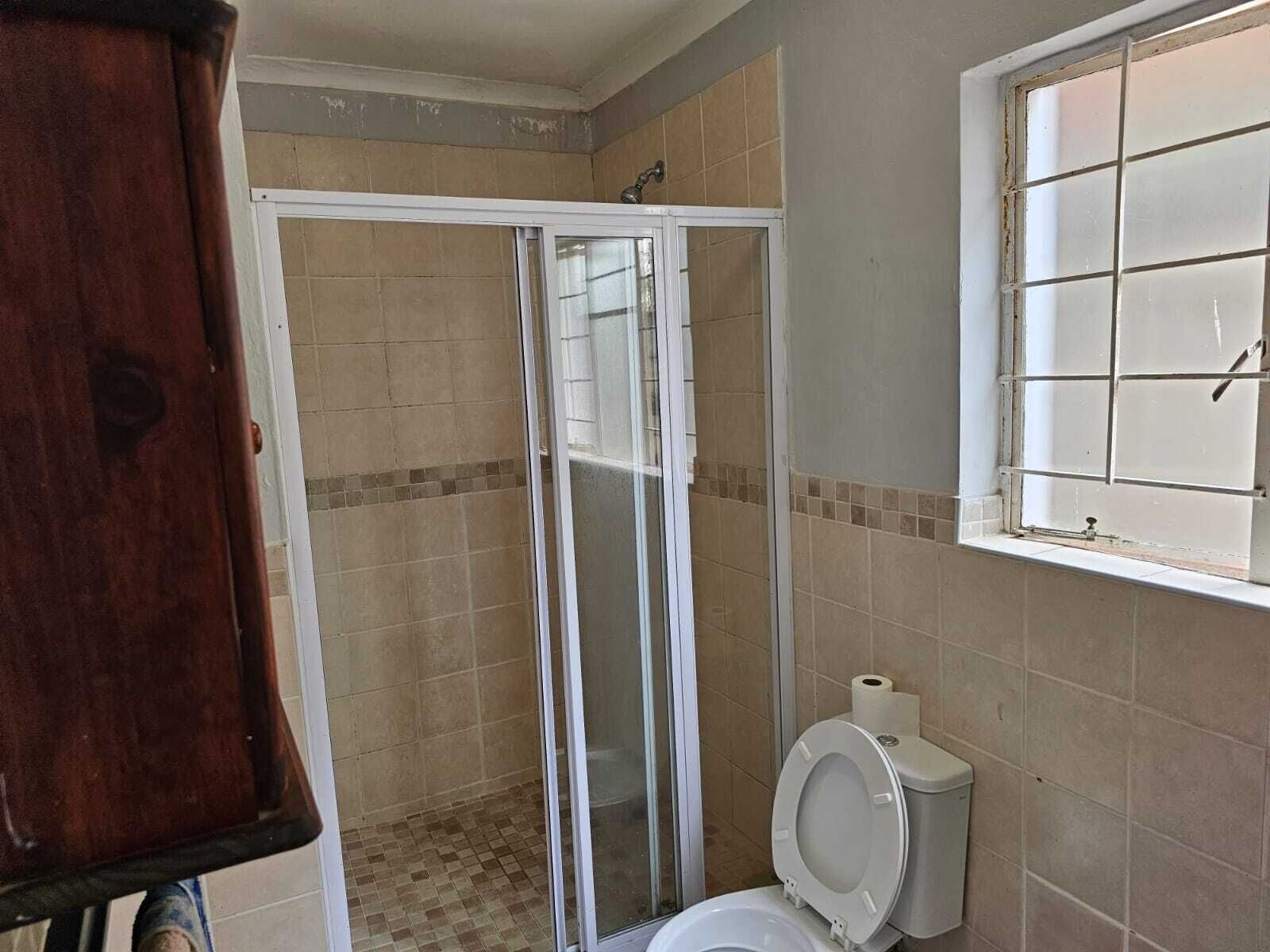 Een badkamer met een douchecabine, toilet en een raam met tralies.