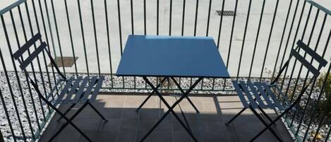 A blue table and two chairs set up on a tiled patio with a metal fence.