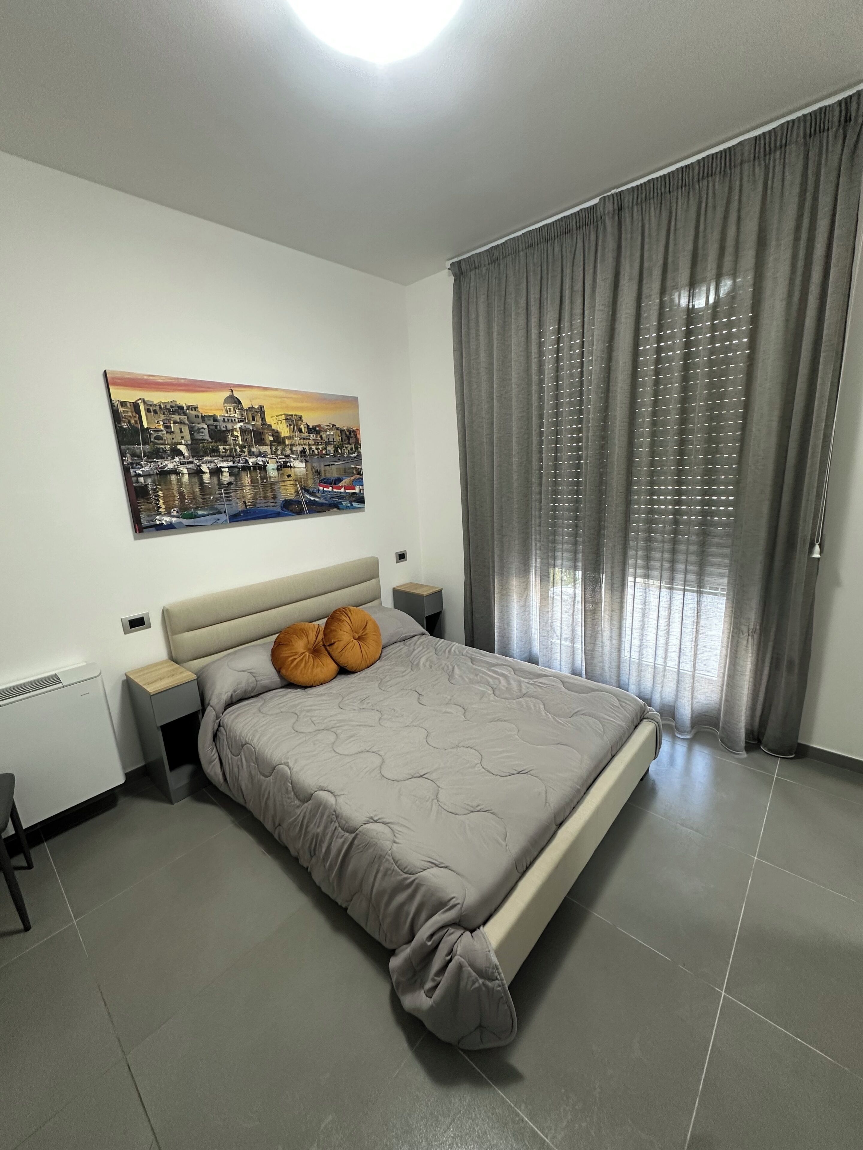 A bedroom with a bed, a nightstand, a wall-mounted painting, and a window with curtains.