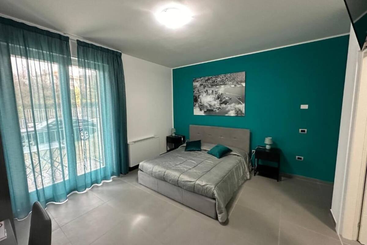 A bedroom with a bed, a nightstand, a window with curtains, and a wall-mounted picture.