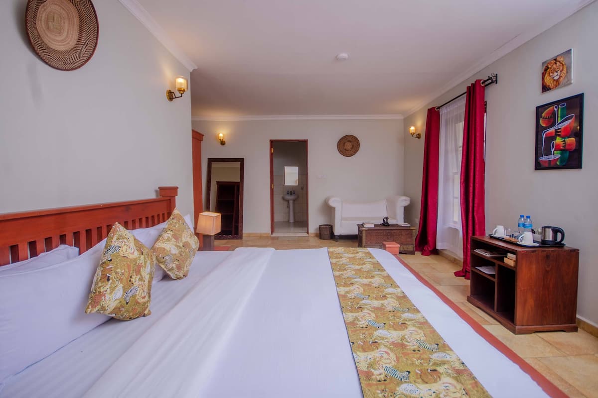 A hotel room with a bed, a nightstand, a wooden side table, a bathroom visible through an open door, and a red curtain.
