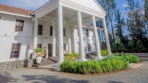 A white building with a central porch supported by columns, surrounded by greenery and a clear blue sky. - Amani Safari lodge  (Arusha)