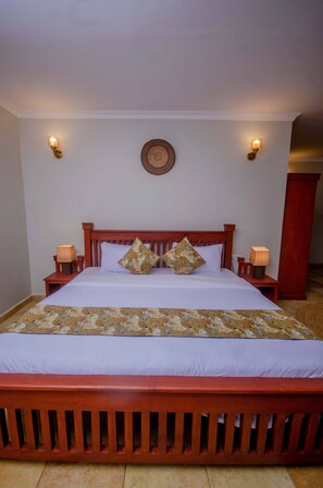 A bed with a wooden headboard, two bedside tables with lamps, and a patterned bedspread. - Amani Safari lodge  (Arusha)