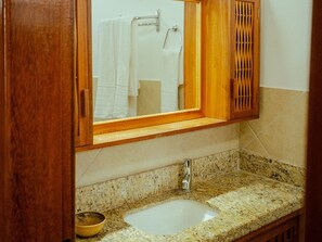 A bathroom with a granite countertop, a white sink, and a wooden cabinet. - House in a gated community with a pool – 300 meters from Taperapuã Beach (Porto Seguro)