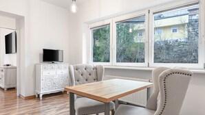 A modern kitchen with a wooden table and chairs, a white cabinet, and a large window with a view of trees. - Geräumiges 39 m² Apartment für 2–3 Personen (Alpenresidenz (Bad Gastein))