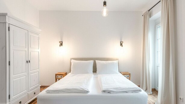 A neatly made bed in a room with wooden flooring, a wardrobe, and two bedside tables with lamps. - Geräumiges 39 m² Apartment für 2–3 Personen (Alpenresidenz (Bad Gastein))
