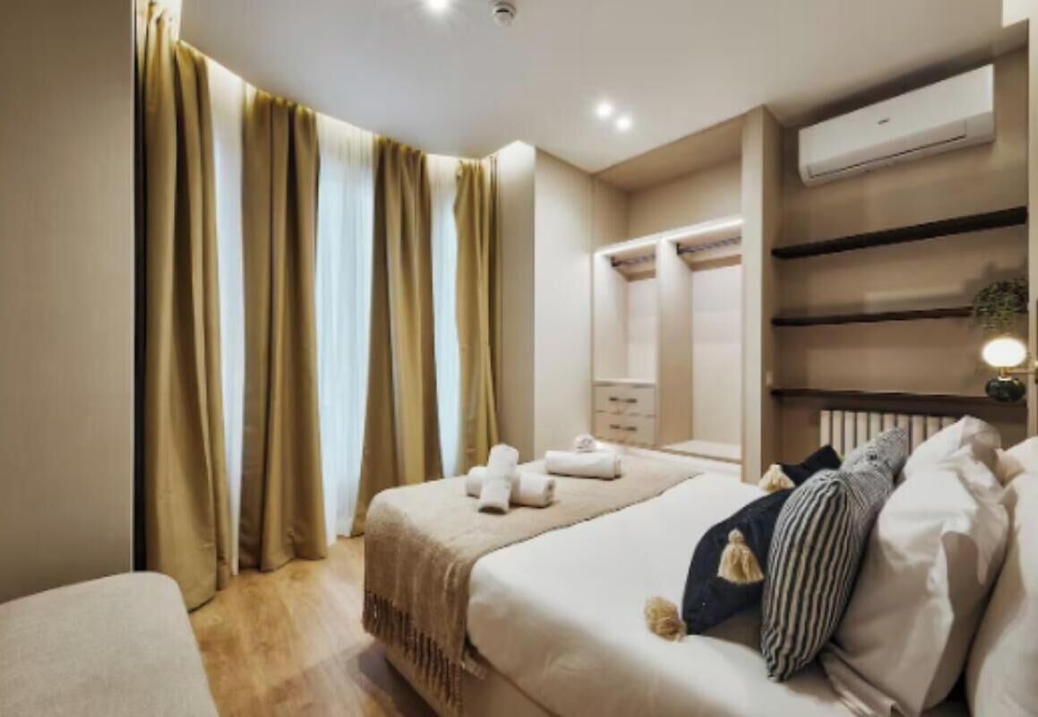 A hotel room with a bed, a wardrobe, a bedside table, and a window with curtains.