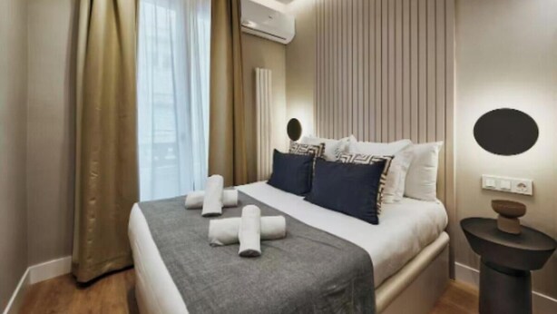Ein modernes Hotelzimmer mit Bett, Vorhängen, einer Klimaanlage, einem Nachttisch und einer Wandleuchte.
