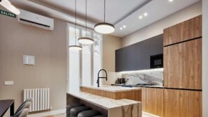 Eine moderne Küche mit Marmorarbeitsplatte, schwarzen Barhocker, Pendelleuchten und einem eingebauten Backofen.