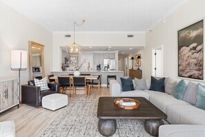 A modern living room with a sofa, coffee table, and dining area. - Sterling Beach 1202 Luxury Beachfront, Heated Pool, Walk in Shower, FREE Golf (Panama City Beach)