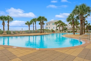 A swimming pool with palm trees and a building in the background. - Sterling Beach 1202 Luxury Beachfront, Heated Pool, Walk in Shower, FREE Golf (Panama City Beach)