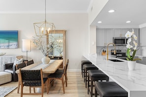 A modern kitchen with a white marble countertop, a built-in oven, and a stainless steel range hood. - Sterling Beach 1202 Luxury Beachfront, Heated Pool, Walk in Shower, FREE Golf (Panama City Beach)