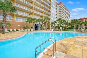 A hotel pool area with a clear blue pool, palm trees, and a multi-story building with balconies. - Sterling Beach 1202 Luxury Beachfront, Heated Pool, Walk in Shower, FREE Golf (Panama City Beach)