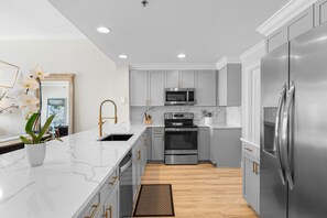 A modern kitchen with white marble countertops, stainless steel appliances, and light gray cabinetry. - Sterling Beach 1202 Luxury Beachfront, Heated Pool, Walk in Shower, FREE Golf (Panama City Beach)
