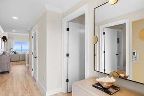 A modern hotel room with a large mirror, a wooden side table, and a view of the sea through the balcony. - Sterling Beach 1202 Luxury Beachfront, Heated Pool, Walk in Shower, FREE Golf (Panama City Beach)