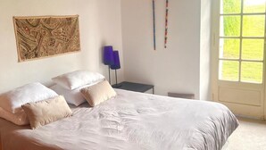 Een slaapkamer met een groot bed, een wandtapijt en een raam met uitzicht op groen.
