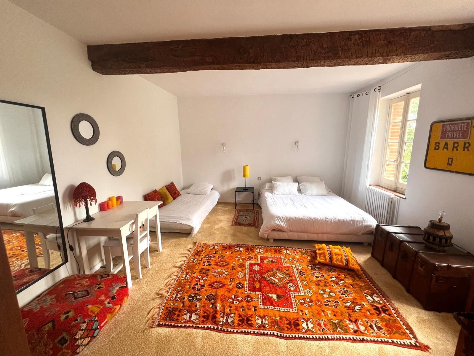 A bedroom with a bed, a desk, a chair, a mirror, a radiator, and a window.
