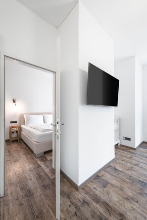 A modern hotel room with a bed, a bedside table, a TV mounted on the wall, and a wooden floor. - Großzügiges 44 m² Apartment mit Balkon für 2–4 Personen (Alpenresidenz (Bad Gastein))