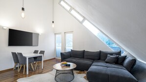 En modern lägenhet i loftstil med ett matområde, en stor grå hörnsoffa, ett runt soffbord och en vit matta av kohud.