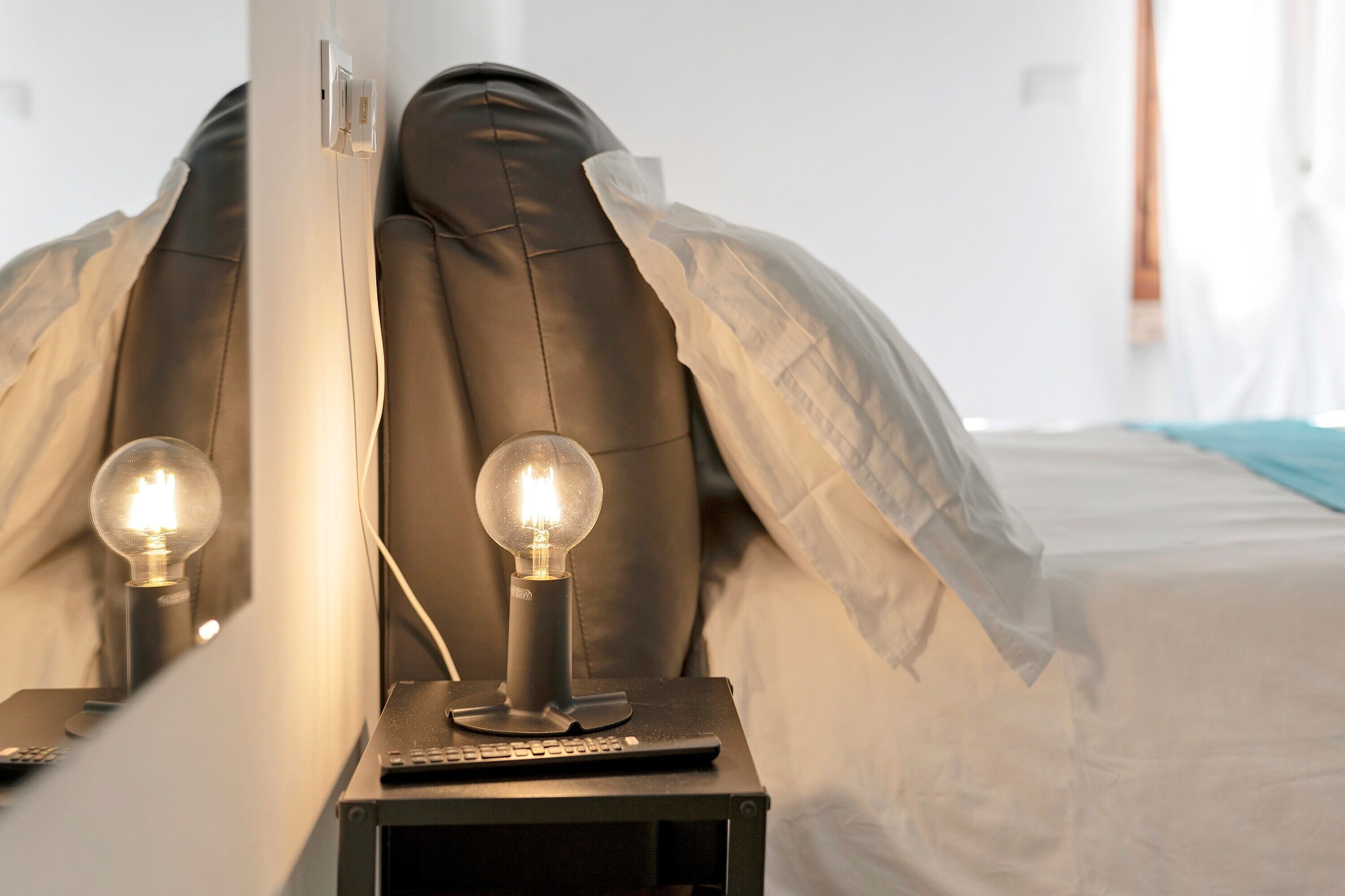 Ein Bett mit Kopfteil, ein Nachttisch mit Lampe und einer Fernbedienung.