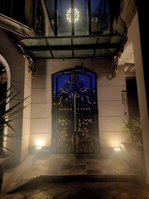 A building entrance with a decorative metal gate, a glass canopy, and a small light fixture on the ground. - L’Ancienne Pierre: A Timeless Masterpiece (Lahore)