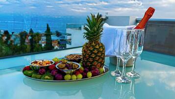 Een tafel met een fruitschaal, een ananas en twee champagneglazen op een balkon met uitzicht op de oceaan.