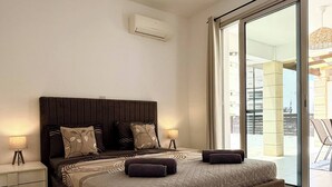A modern bedroom with a large bed, two bedside tables, and a sliding glass door leading to an outdoor area. - Amáni Seaview 3 Bedrooms Luxury Villa (Pegeia)