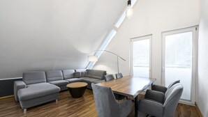 Eine moderne Lofts-Wohnung mit geneigter Decke, einem Ecksofa, einem Holzesstisch und einem großen Fenster, das für natürliches Licht sorgt.