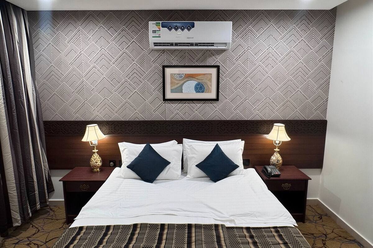 Ein Hotelzimmer mit einem großen Bett, zwei Nachttischen mit Lampen, einer Wandklimaanlage und einem gerahmten Bild über dem Bett.